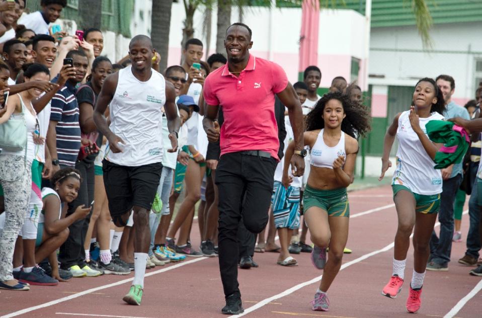 Jamaican sprinter and six-time Olympic gold medallist Usain Bolt (C) runs with children during a visit to a sports complex at the Mangueira shantytown in Rio de Janeiro, on April 16, 2015 (Photo via AFP/Vanderlei Almeida)
