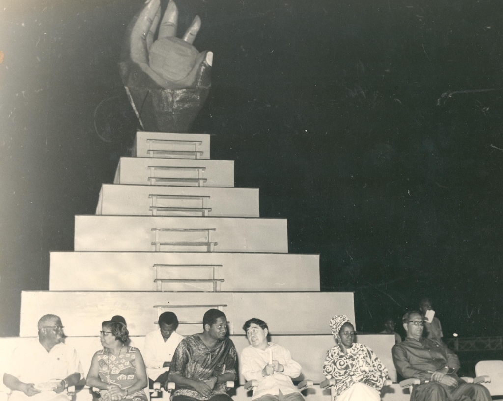 At the closing ceremony of CARIFESTA 1972 is the CARIFESTA logo - a dark hand grasping the sun, depicting the skills and aspirations of the tropical man with talent untold'.  In the foreground are (second and third from left respectively) then Prime Minister of Guyana, Linden Forbes Sampson Burnham and  then President of Guyana, Arthur Chung.